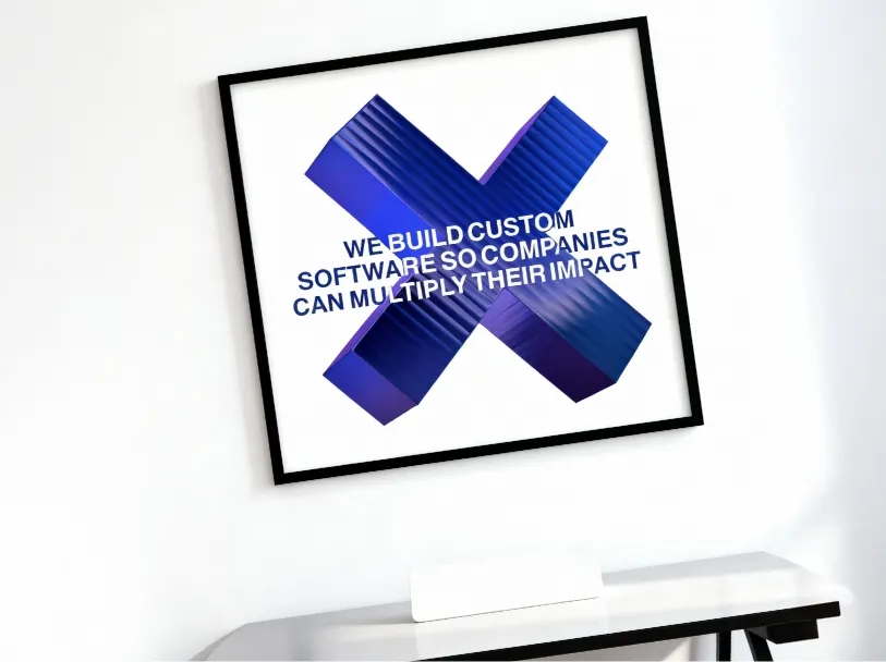A framed artwork featuring a blue 3D "X" and the text, "We build custom software so companies can multiply their impact."